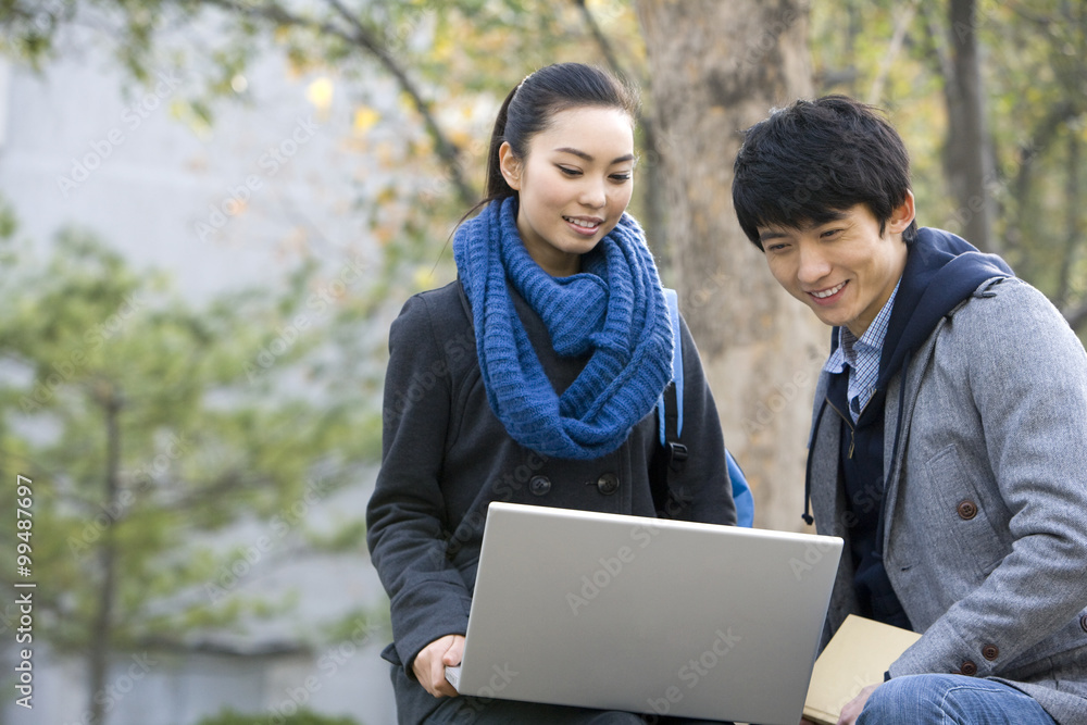 A young man and woman using a laptop together on a park bench