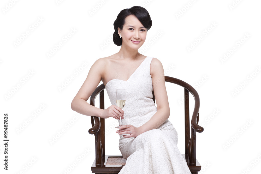 Elegant young woman sitting on Chinese Ming-style wooden armchair with champagne flute