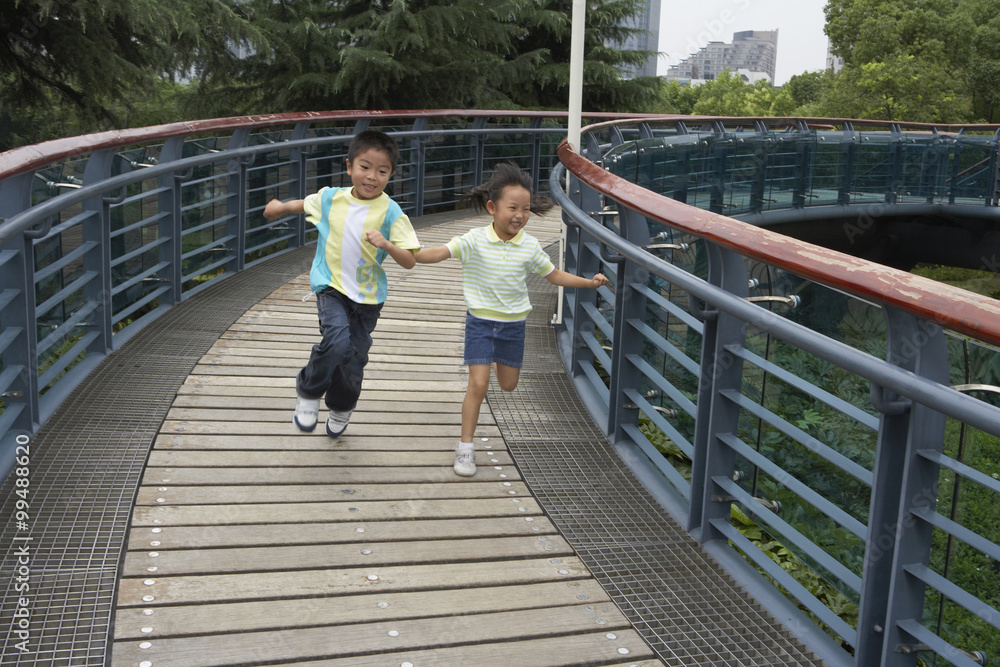 年轻男孩和年轻女孩在公园里跑过桥