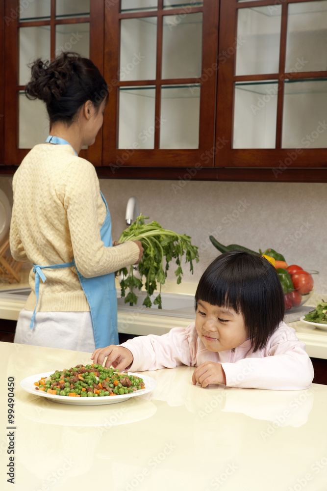 年轻女孩一边吃蔬菜，一边妈妈做饭