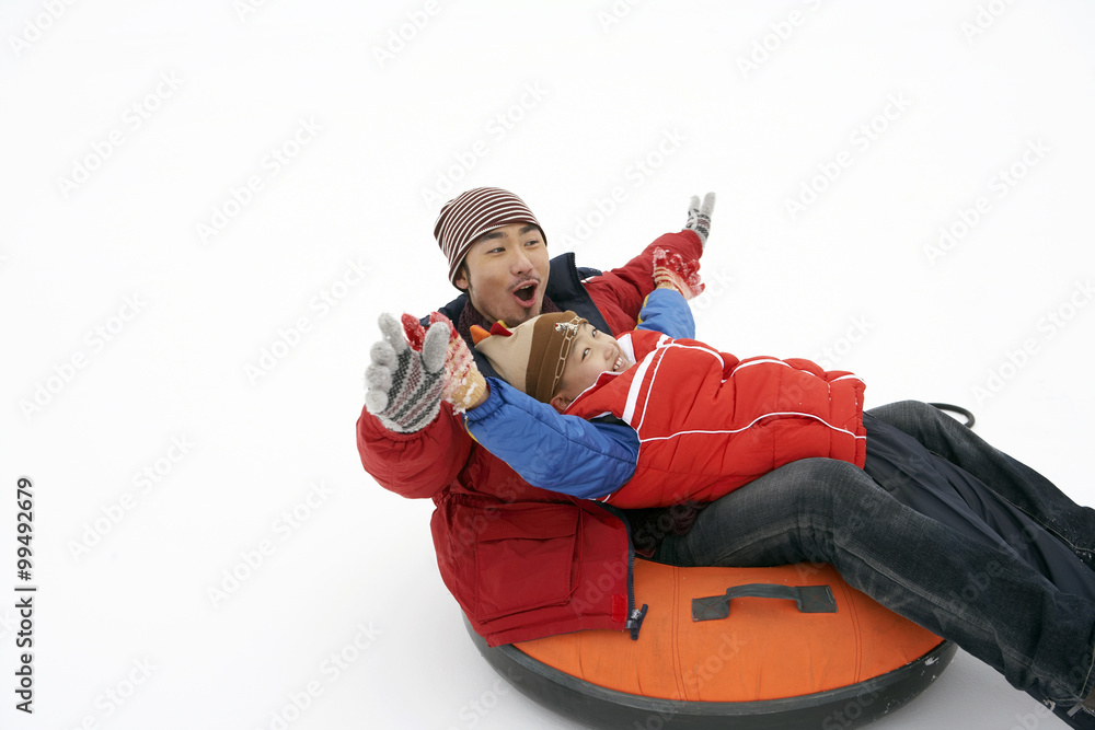 Father And Son Riding On Inflatable Snow Tube