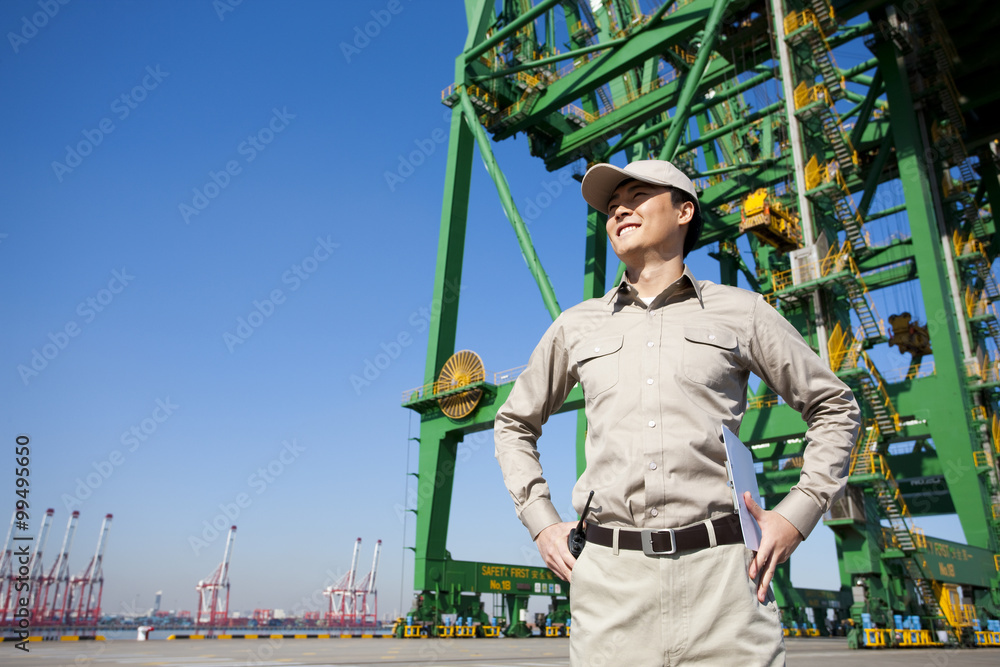 Male shipping industry worker with hands on hips with shipping dock background