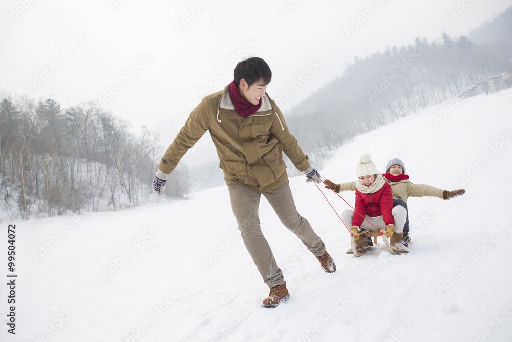 Young father pulling his children on sled