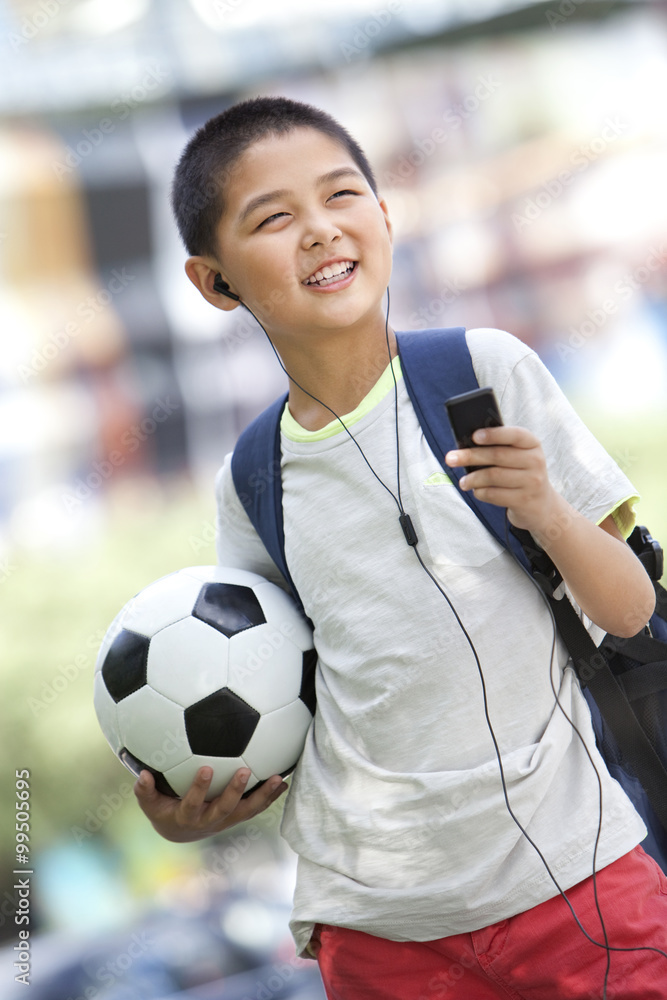 Schoolboy listening to MP3 player with football in hand