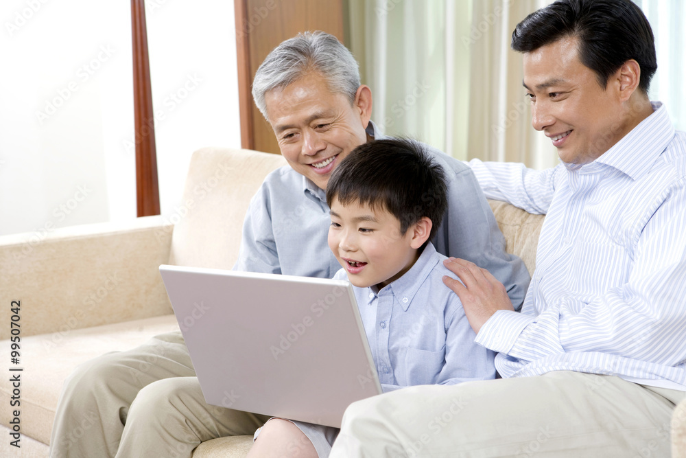 Grandfather, father, and son use laptop on a sofa