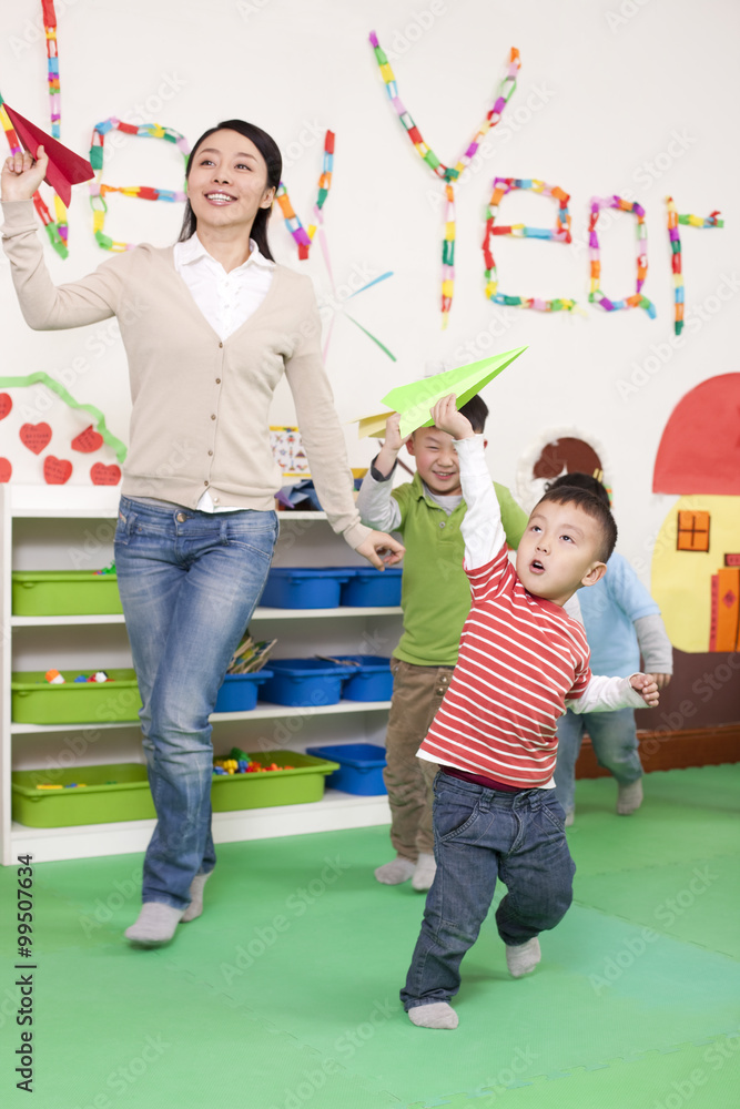 Lovely kindergarten children flying paper planes with teacher