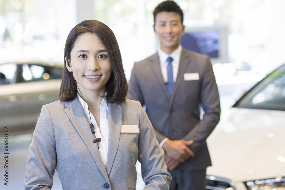 Confident salespeople standing with new cars in showroom