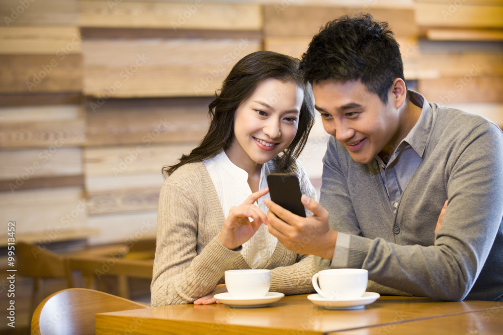 Happy young couple with smart phone in cafe