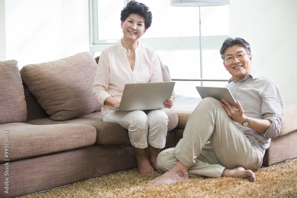 Happy senior couple with laptop and digital tablet