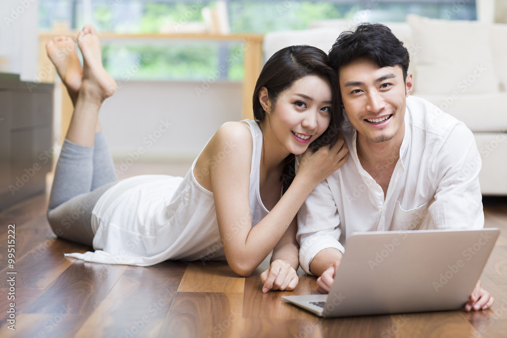 Young couple lying on floor using laptop