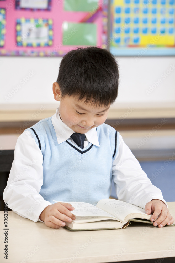 Young boy reading at his desk in a classroom