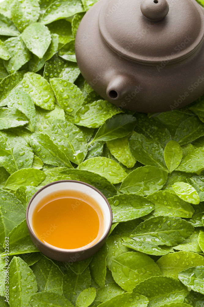 Teapot and cup of tea on green leaves