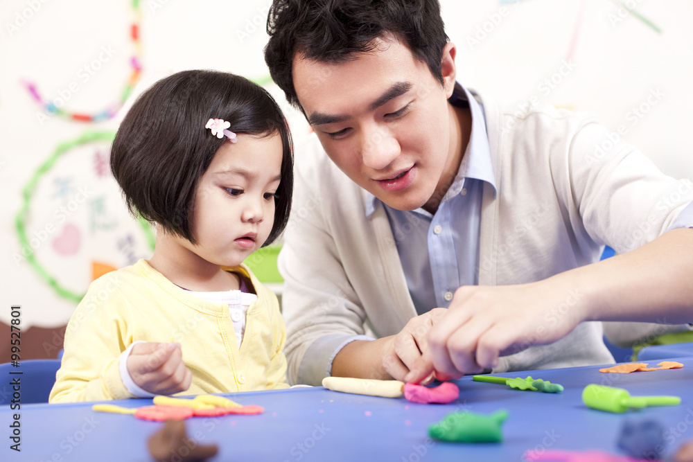 Kindergarten teacher and lovely girl playing with childs play clay