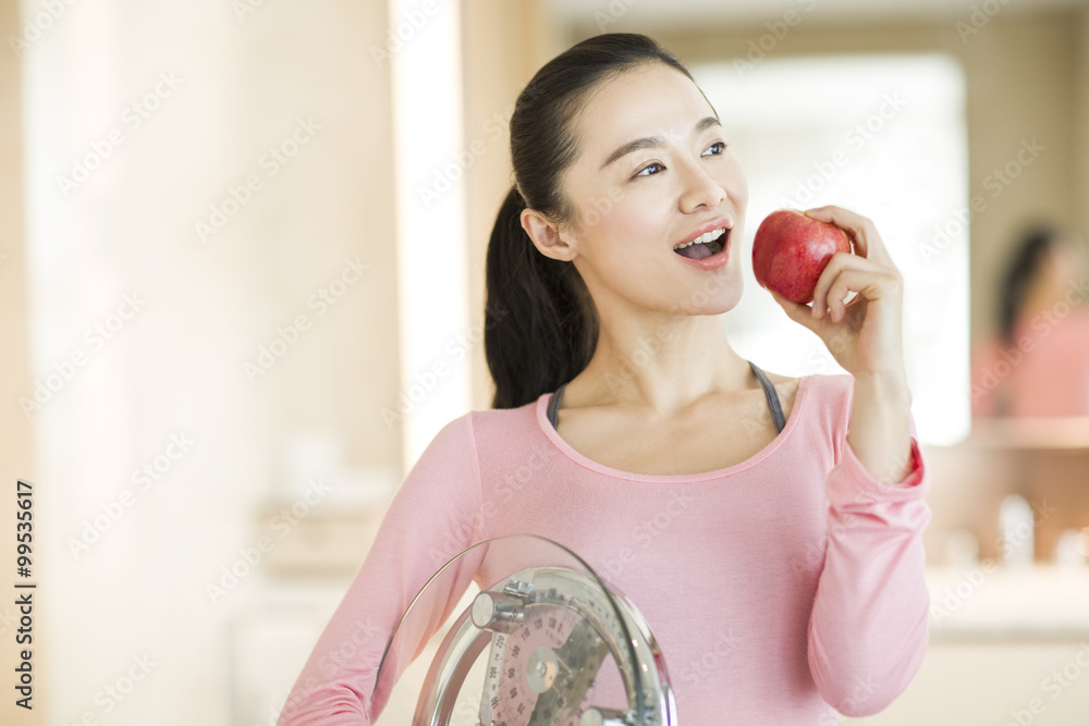 Happy young woman holding weight scale and apple