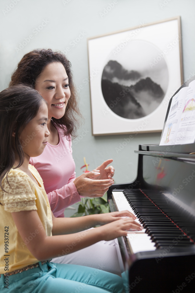 Mother teaching daughter to play the piano