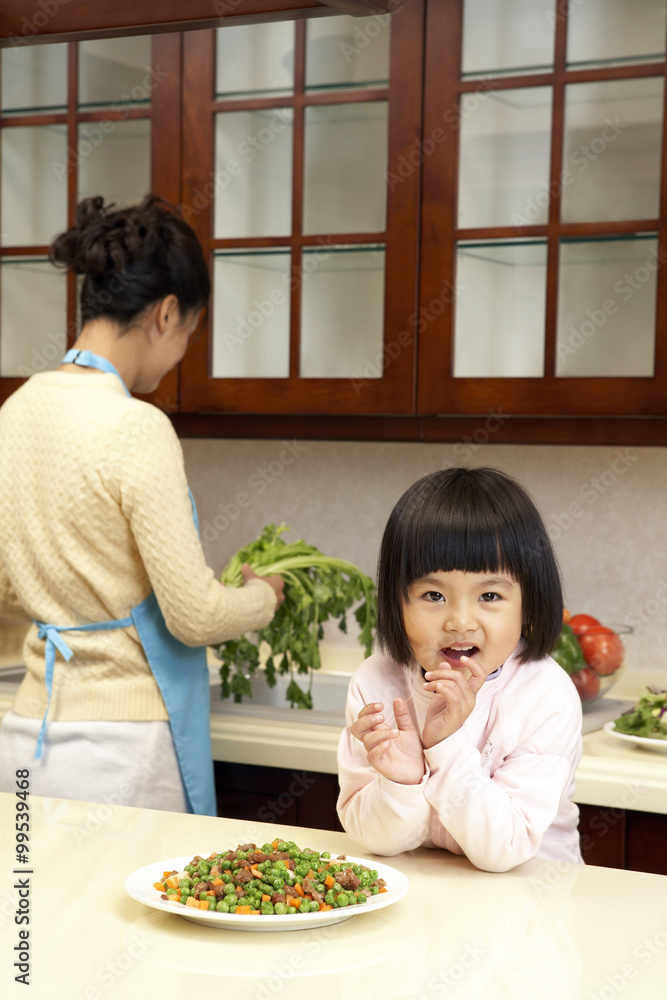 年轻女孩一边吃蔬菜，一边妈妈做饭