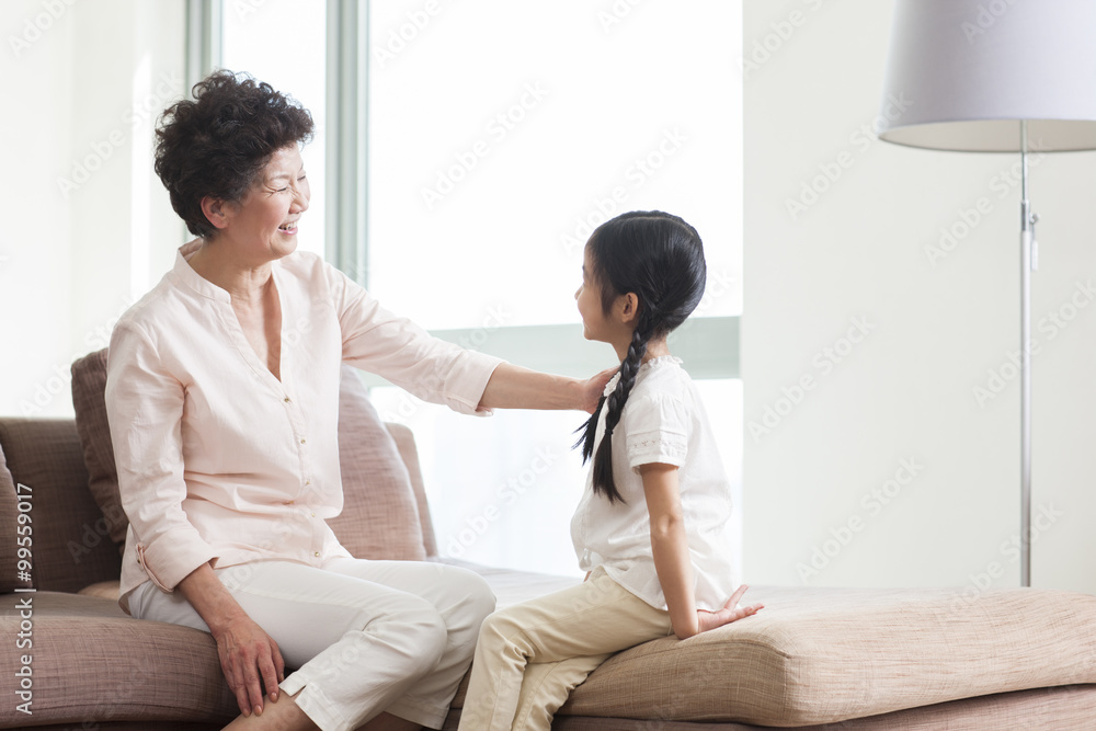 Happy grandmother and granddaughter sitting in sofa