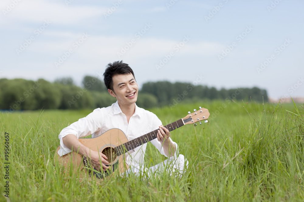 Happy young man playing guitar on the grass