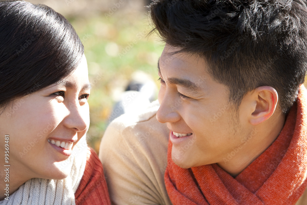 Young couple lying on the grass surrounded by Autumn leaves