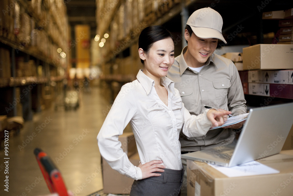 Chinese businesswoman in a warehouse with worker using a laptop