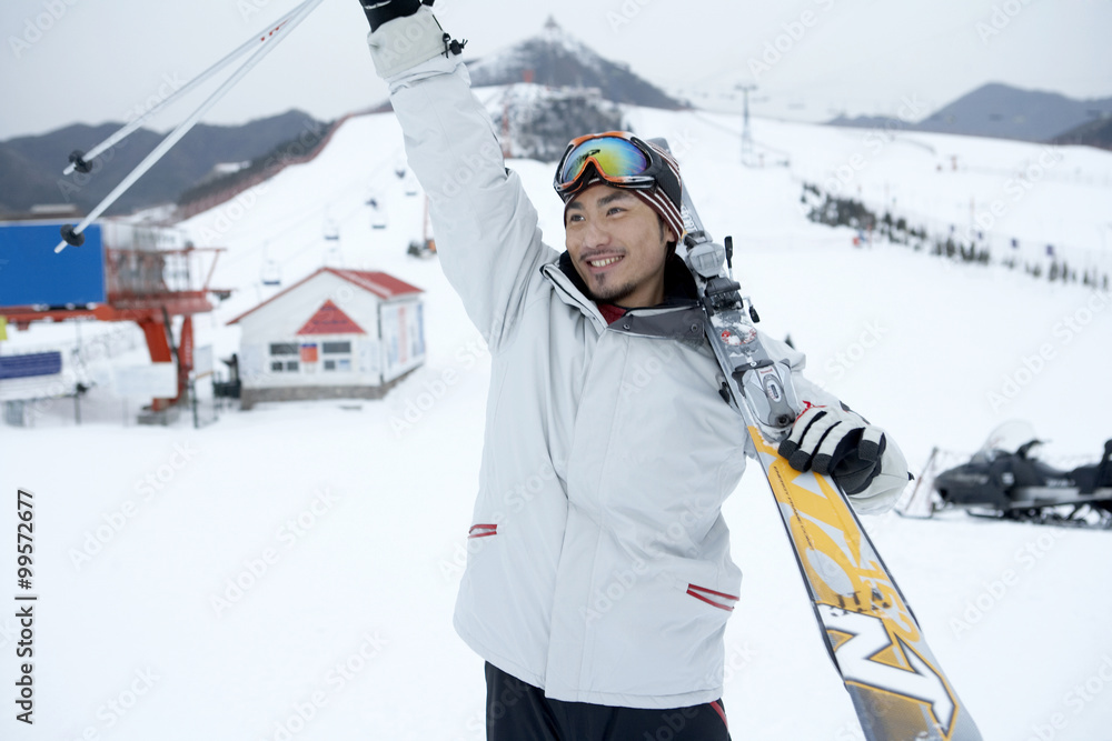 男子在滑雪场上举着滑雪板和滑雪杆