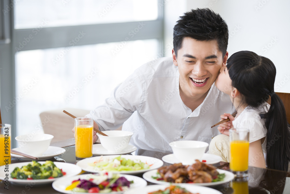 Happy daughter kissing father on the cheek during lunch