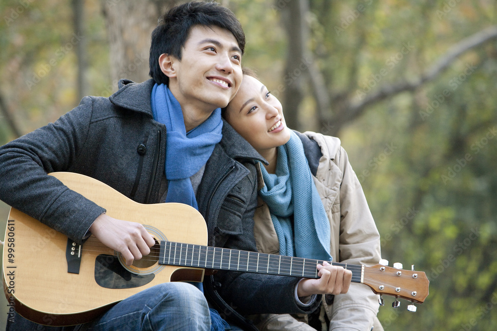 A young man plays the guitar as he girlfriend leans on him affectionately