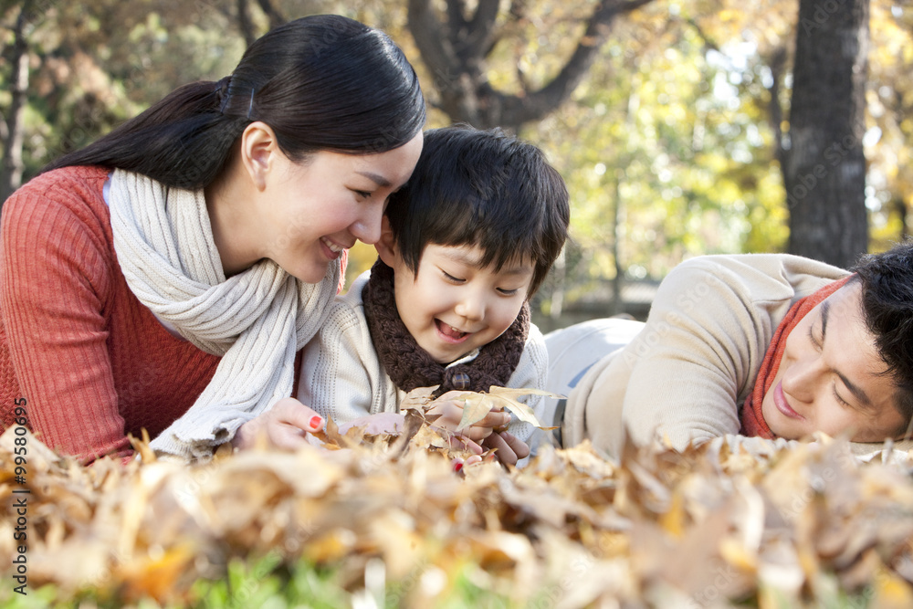 Young family lying on the grass surrounded by Autumn leaves