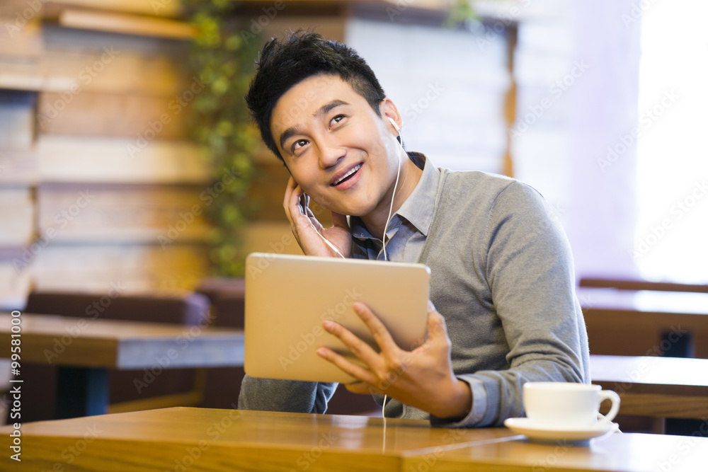 Young man enjoying music in digital tablet in coffee shop