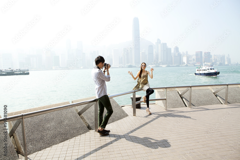 Happy young man photographing young women with SLR camera in Victoria Harbor, Hong Kong