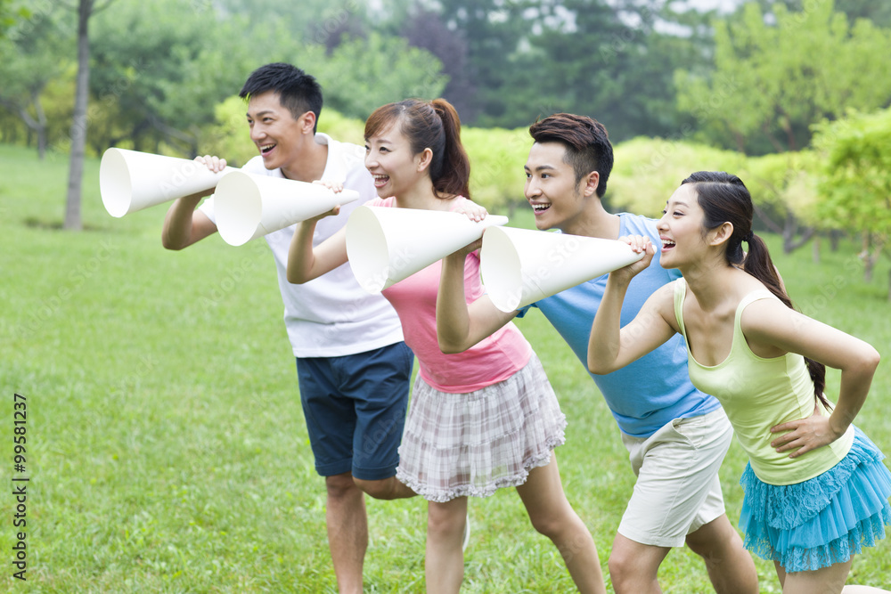 Cheerful young people using megaphones in park