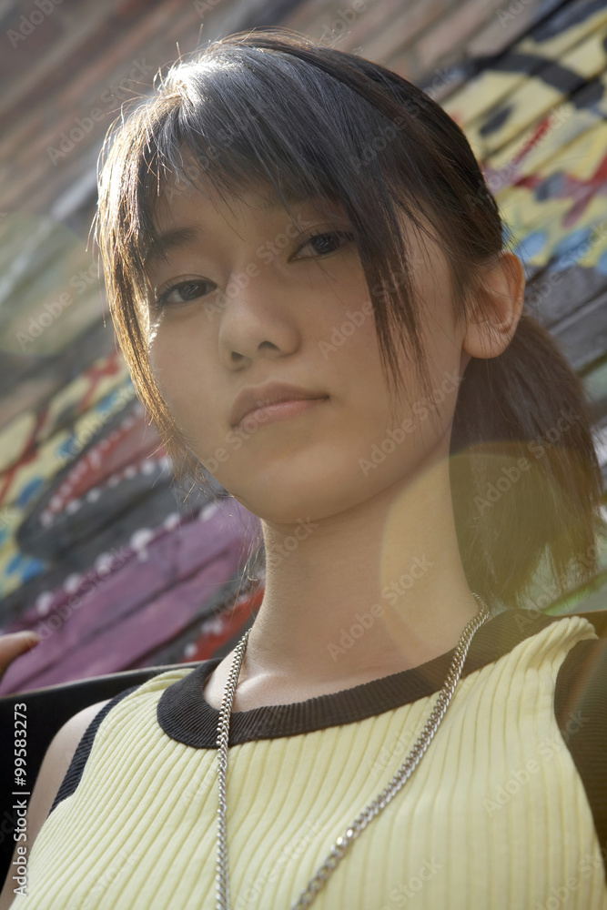 Teenage Girl With Skateboard Leaning On A Wall Of Graffiti