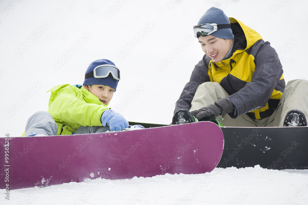 年轻的父子在雪地上玩滑雪板