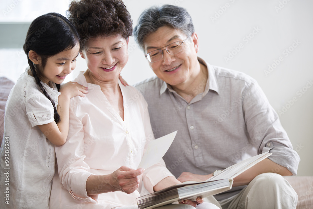 Happy grandparents and granddaughter looking at photo album