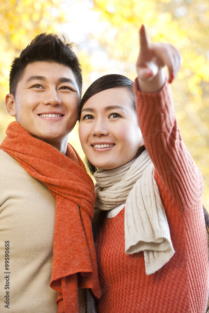 Young couple standing and pointing with Autumn leaves in the background