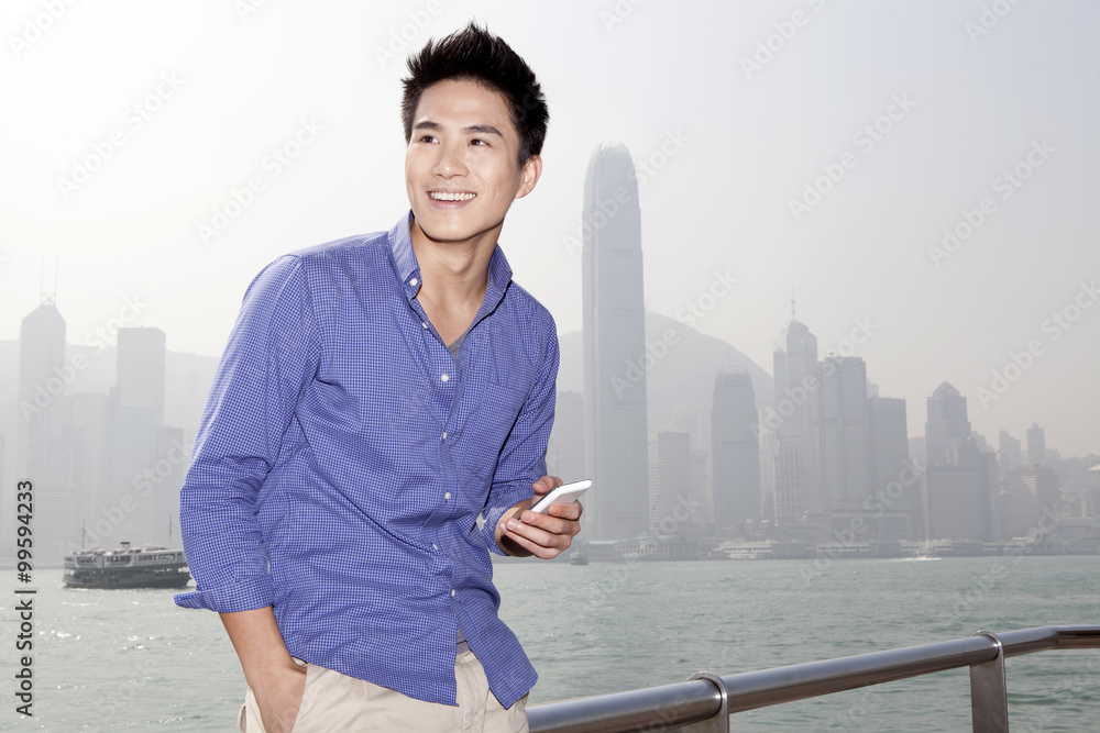 Happy young man with smart phone in Victoria Harbor, Hong Kong