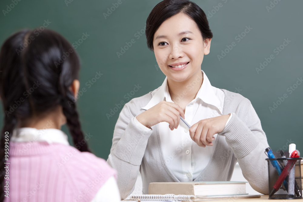 Smiling teacher and schoolgirl having a conversation in classroom