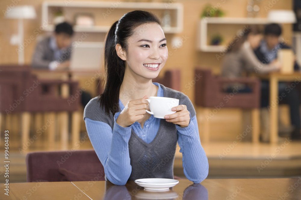 年轻女子在咖啡馆里抱着享受一杯咖啡