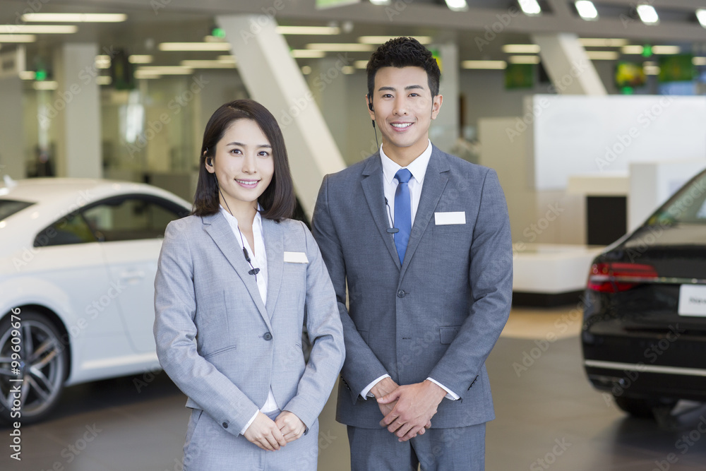 Confident salespeople standing with new cars in showroom