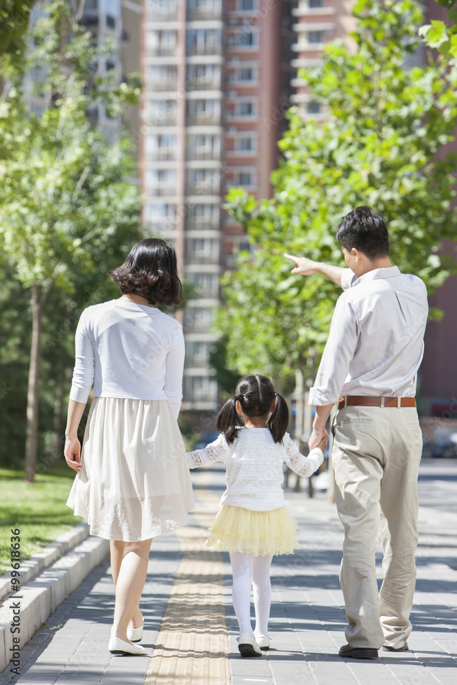 年轻父母带着女儿手牵着手在人行道上漫步