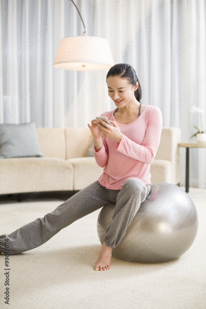 Young woman sitting on fitness ball with smart phone