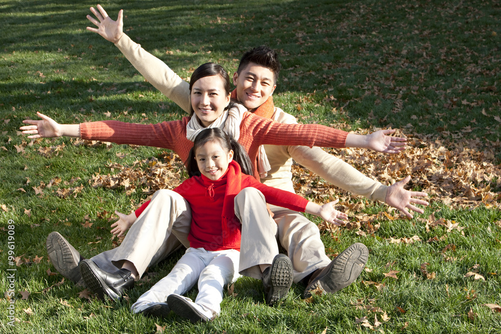 Young family having fun with arms outstretched sitting on the grass