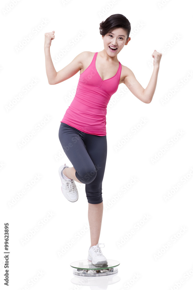 Slim young woman standing on scale and cheering