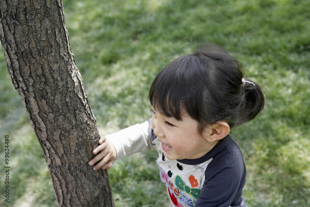 Young Girl Hiding Behind A Tree In The Park