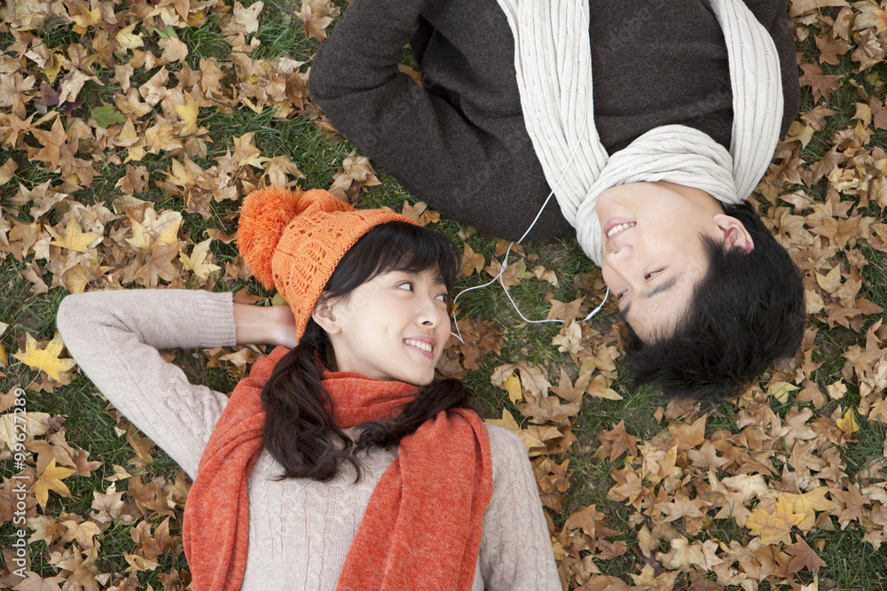 Young Couple Lying Amonst Maple Leaves Listening to MP3 Player