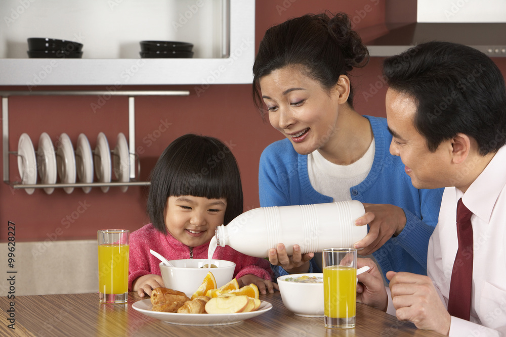 Woman pouring milk for her daughter at the breakfast table