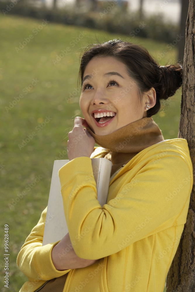 Young Woman Leaning Against A Tree Reading Her Book