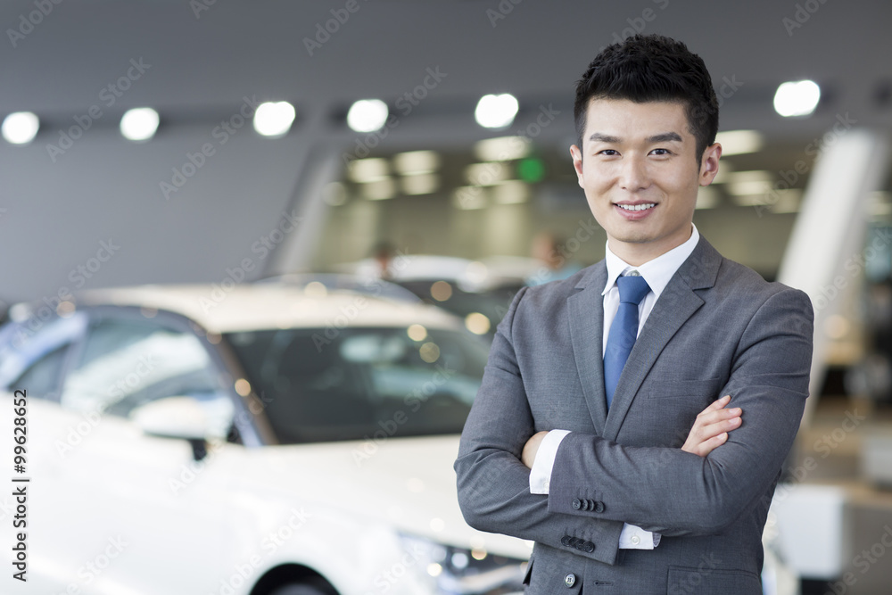 Confident salesman standing with new cars in showroom