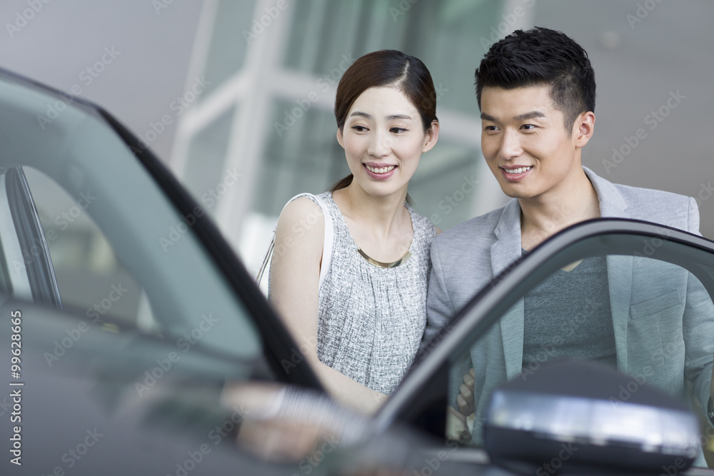 Young couple looking at new car in showroom