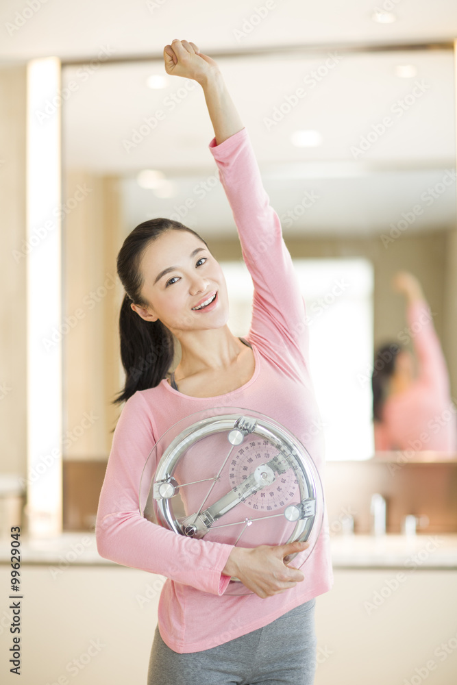 Happy young woman holding weight scale